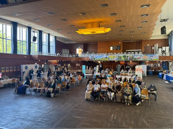Blick in den Veranstaltungssaal mit Publikum vor der Bühne und Ständen an den Seiten