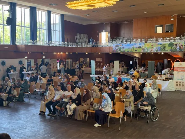 Blick in die Festhalle mit Publikum in Stuhlreihen und Ausstellerständen an den Seiten