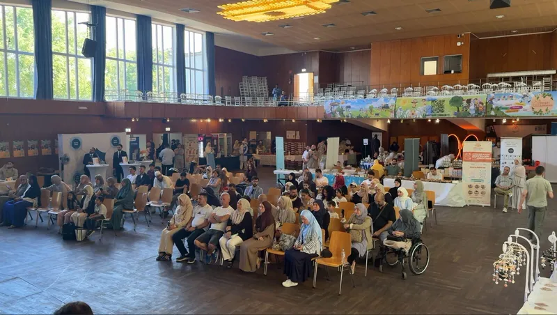 Blick in die Festhalle mit Publikum in Stuhlreihen und Ausstellerständen an den Seiten